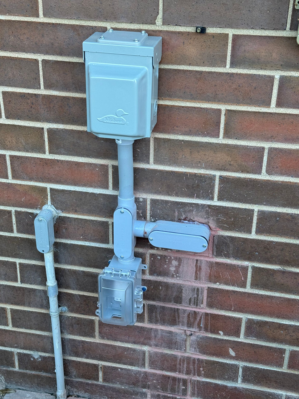 Gray electrical enclosure and conduit mounted on a brick wall
