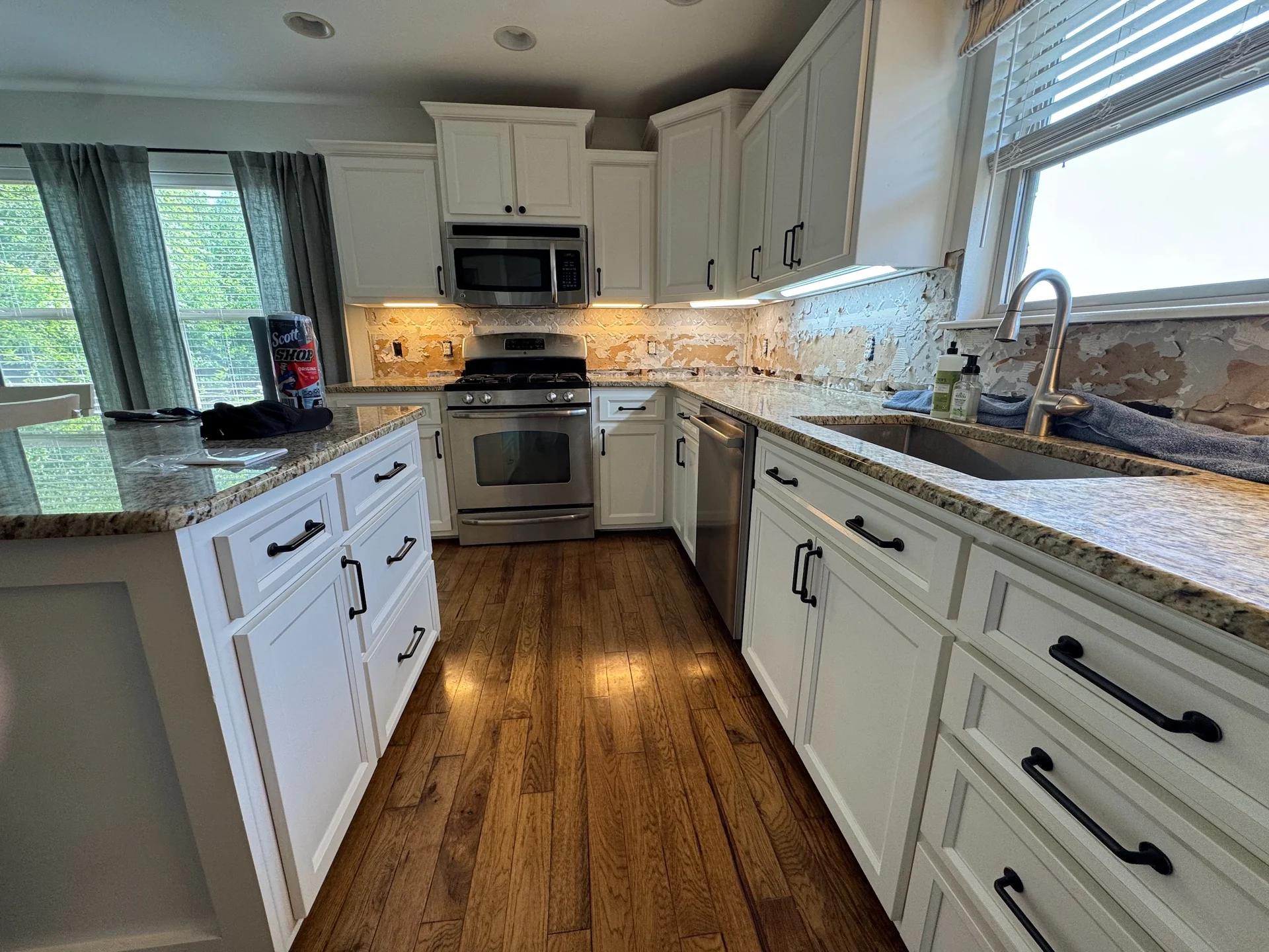Illuminated fixtures beneath white kitchen cabinets during a backsplash renovation