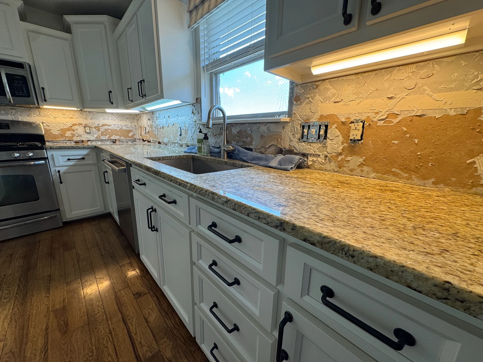 Close view of illuminated under-cabinet fixtures above a kitchen counter and unfinished backsplash