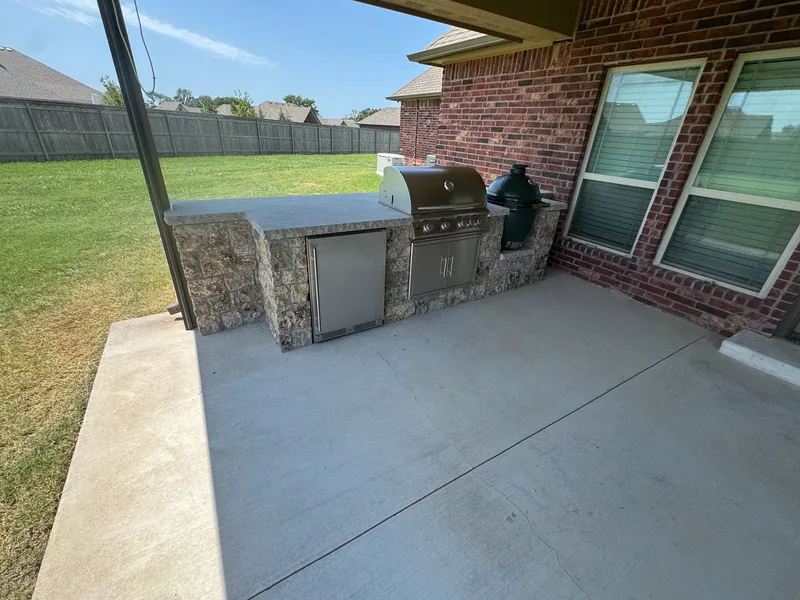 Stone outdoor kitchen and grills beneath a covered brick-home patio with a ceiling fan