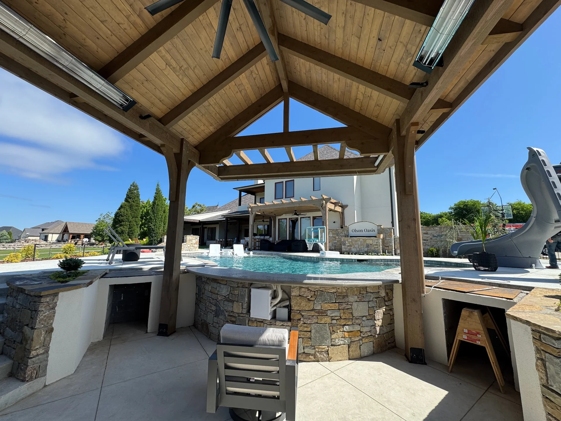 Ceiling fan beneath a timber pavilion above an outdoor kitchen beside the pool