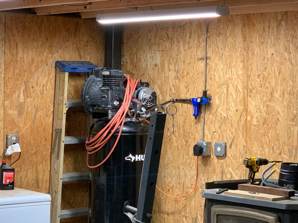 Electrical outlets and conduit beside an air compressor, work area and overhead light in a workshop